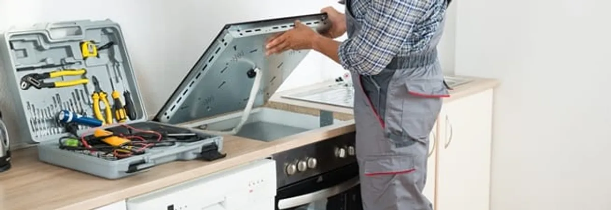 Cooktop repair technician lifting a built-in stovetop for service in Henderson, NV