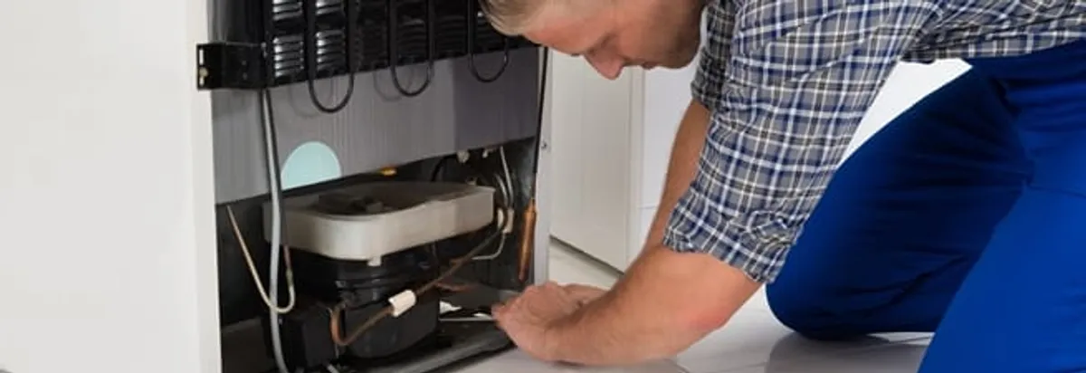 Refrigerator repair technician servicing the compressor and condenser area in Henderson, NV